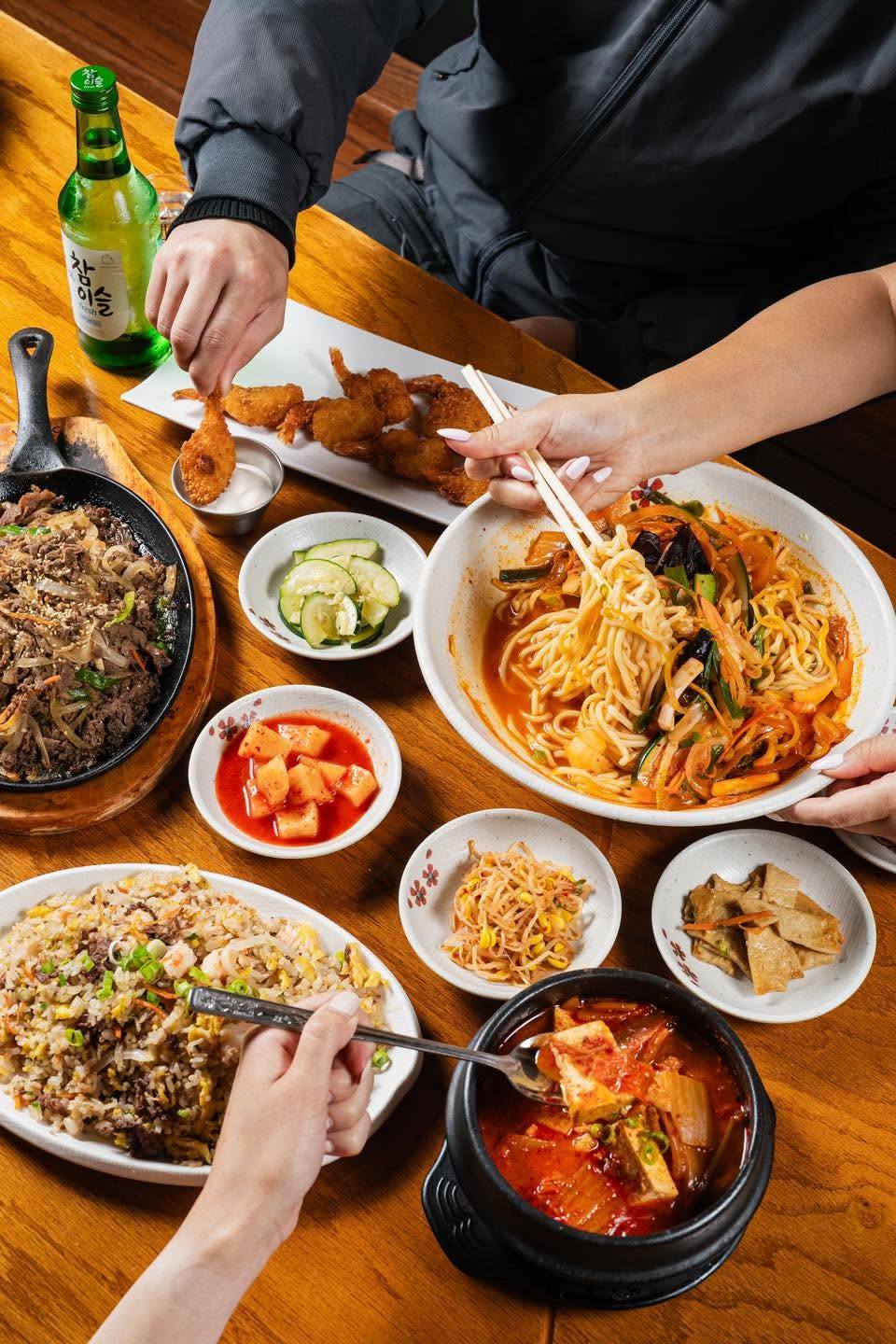 A full table spread of bulgogi, fried rice, noodles, kimchi jjigae, banchan, and soju